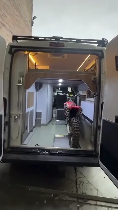 Vista trasera del motorhome con la cama elevada y una moto en el garaje